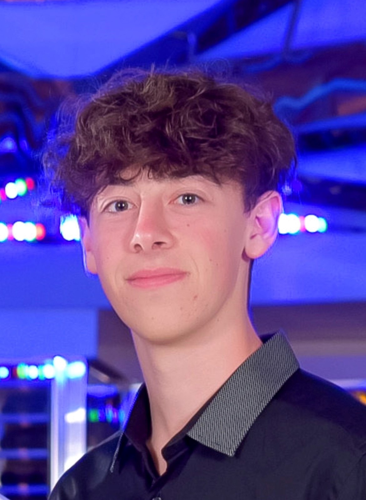 Maximillion Bolkhovsky Person smiling, wearing a black shirt with a background of blurred colorful lights.